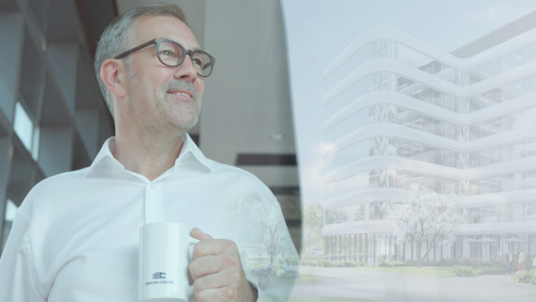 mann steht im office mit kaffeetasse und schaut auf glasgebäude