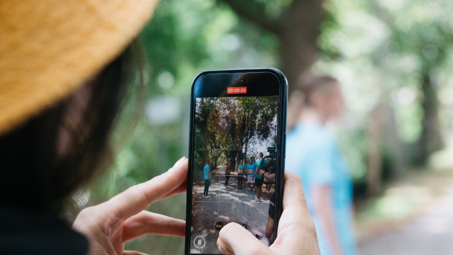 Frau mit gelbem Hut filmt eine Szene im Hochformat mit dem Smartphone